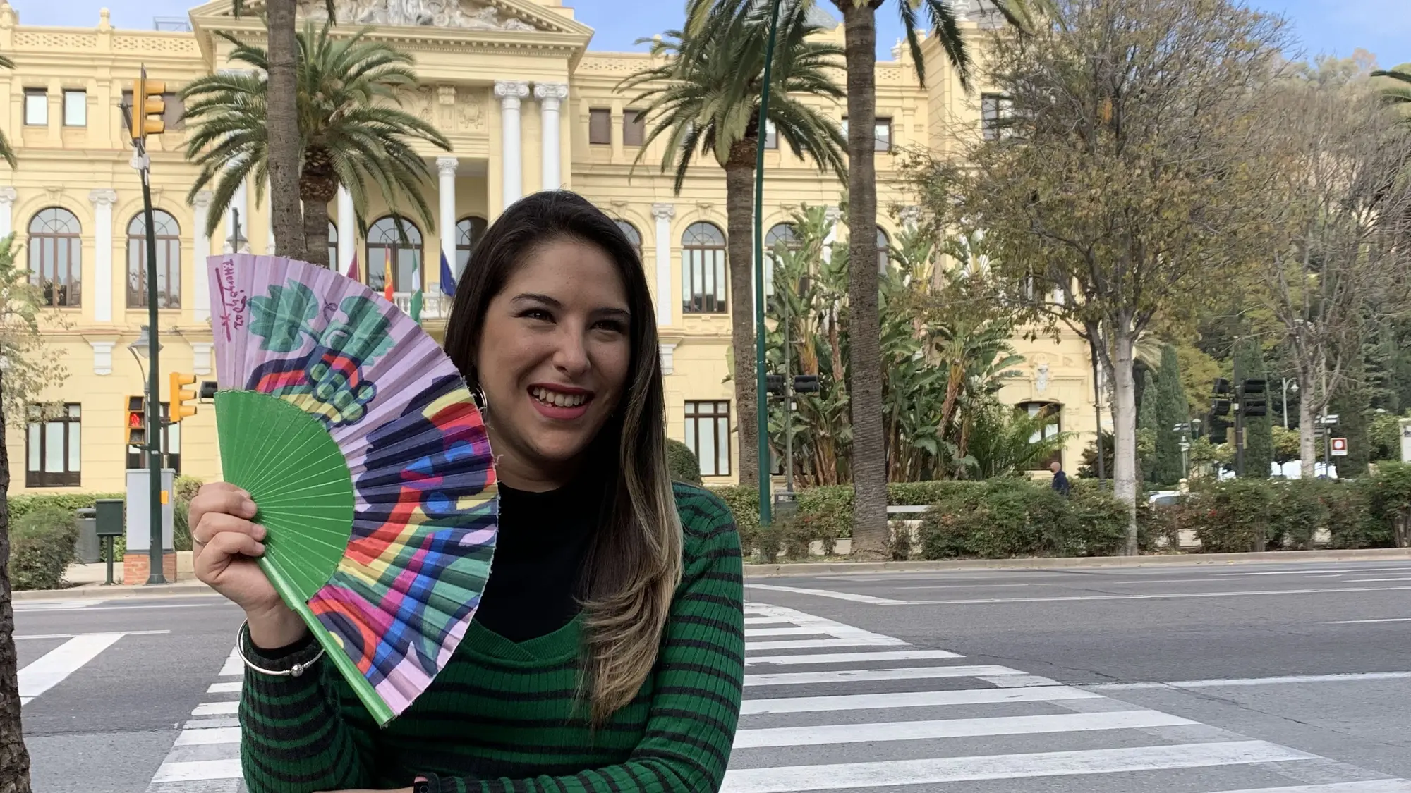 Cris sonriendo con un abanico de colores en una plaza
